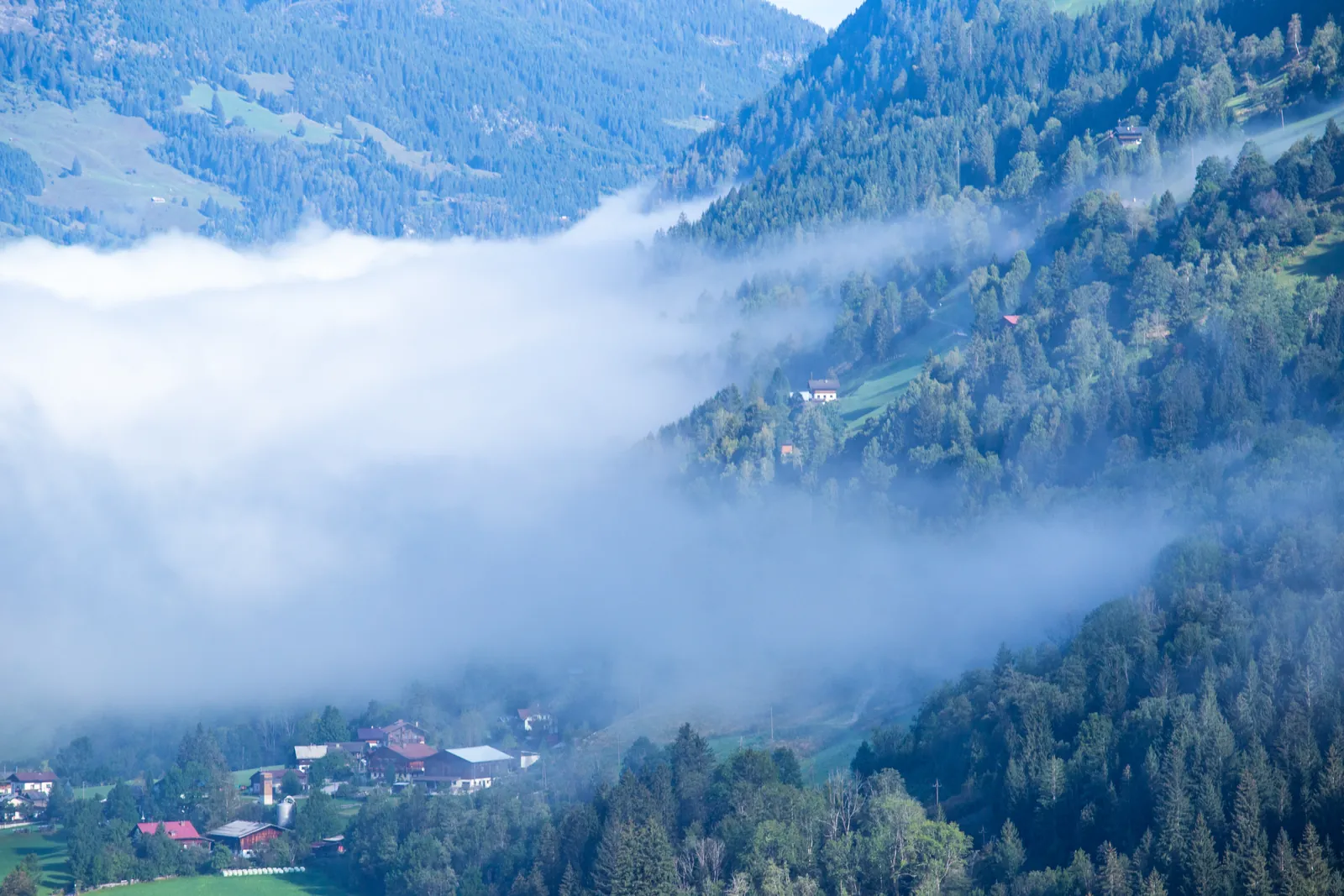 Bad Gastein pod pomalou řekou údolní mlhy při pohledu ze zalesněných svahů nad městem.