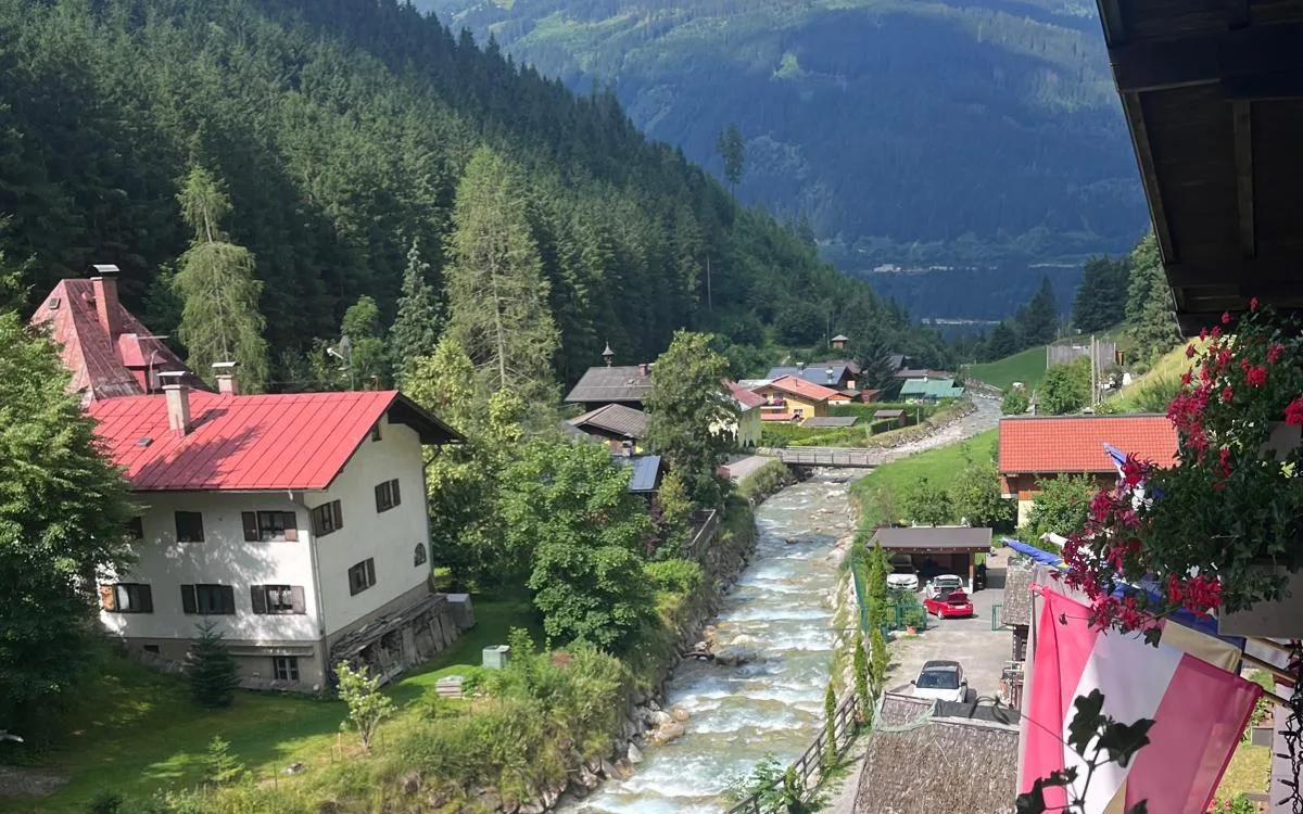 Kötschachtal v létě — potok teče kolem domu a údolí se otevírá do dálky.